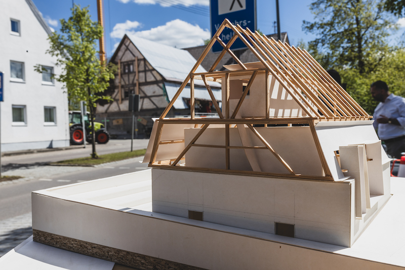 Ein Modell eines Fachwerkhauses im Vordergrund, im Hintergrund ist das gleiche Haus tatsächlich gebaut zu sehen, dazwischen eine Straße.