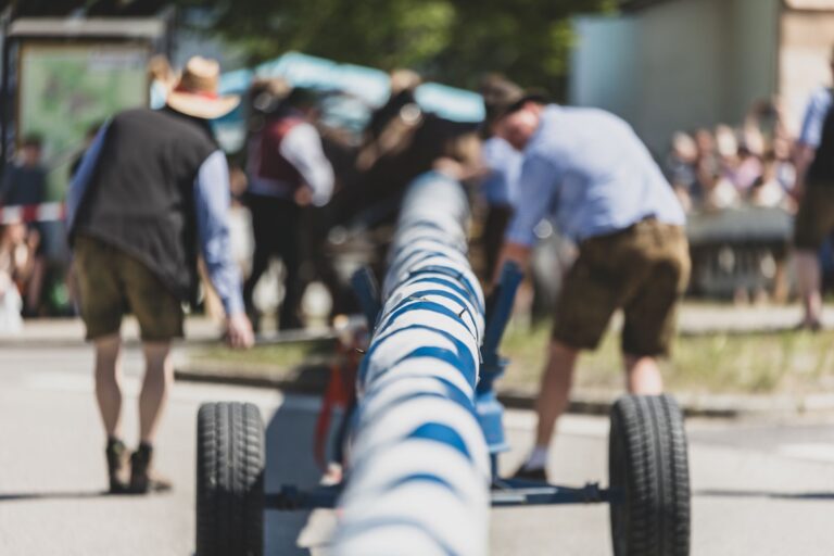 Ein Maibaum wird von Männern in Tracht auf Rädern transportiert.