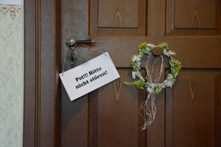 Eine alte Holztüre mit einem kleinen Blumenkranz und einem Schild "Psst, bitte nicht stören"